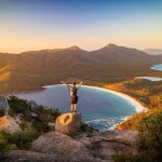 Hiker enjoying panoramic view of Wineglass Bay at sunset, highlighting the good time to visit Tasmania for stunning landscapes