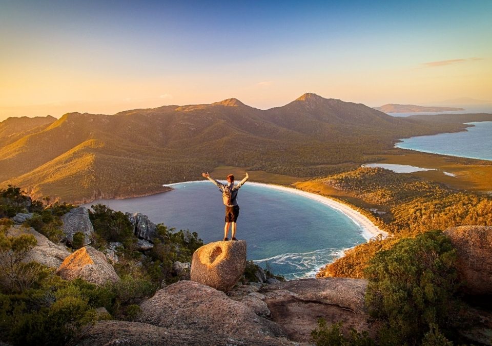 Hiker enjoying panoramic view of Wineglass Bay at sunset, highlighting the good time to visit Tasmania for stunning landscapes